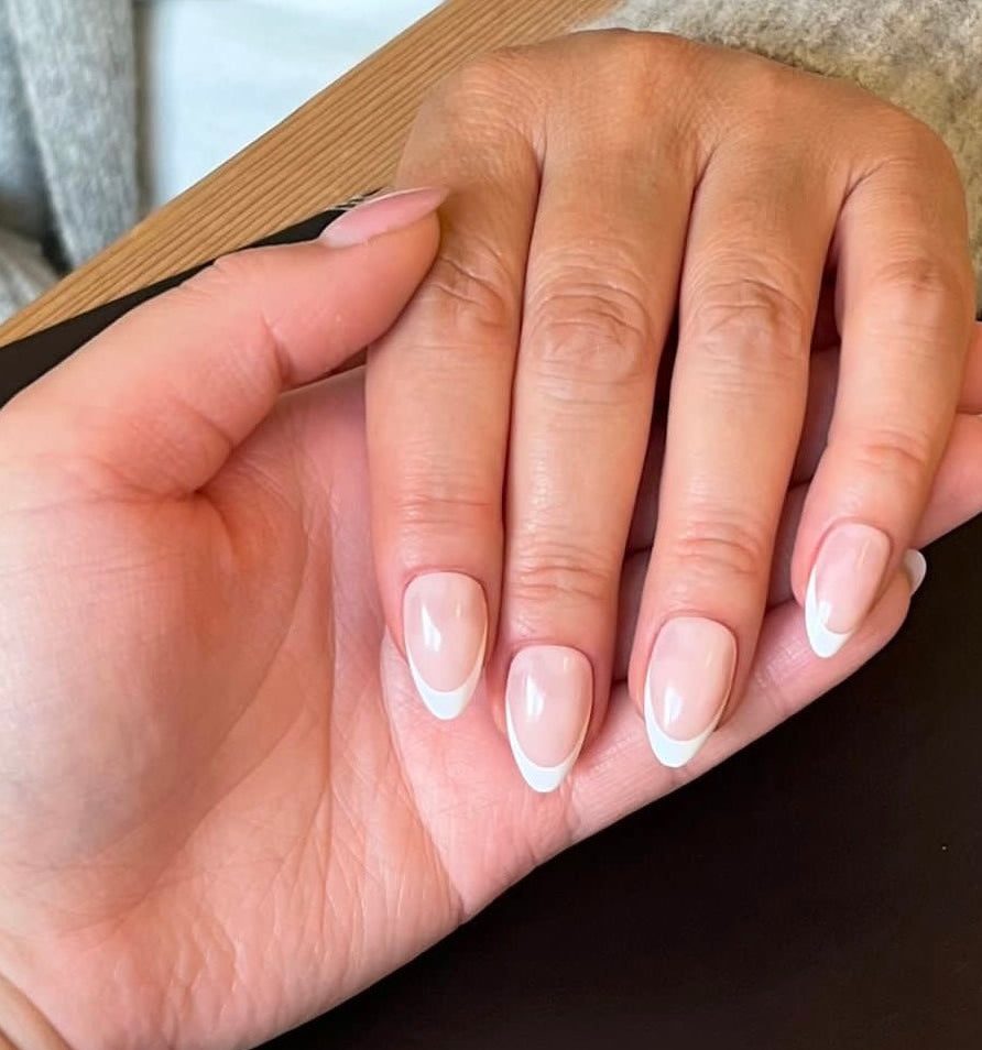 Hand holding another hand showing off decode beauty almond white French tip press on nails 